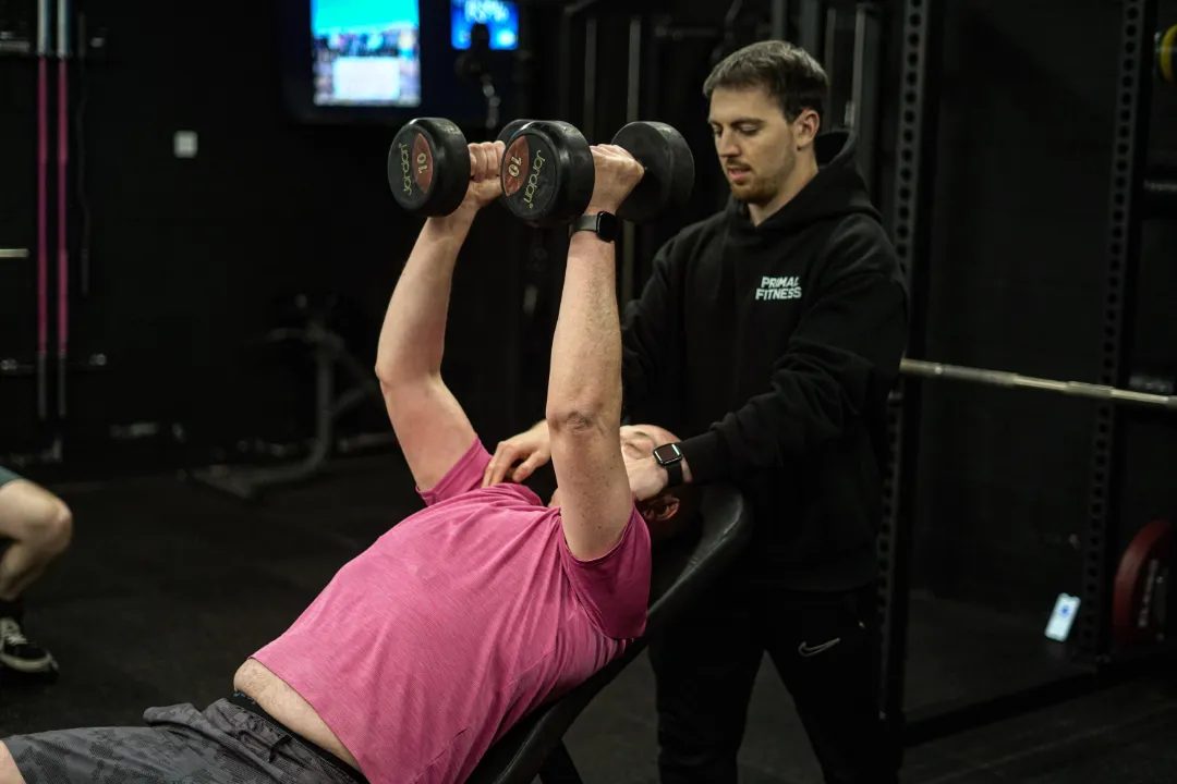 A Primal coach spotting a member on a dumbbell bench press